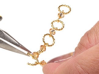 Chain of twisted jump rings alternating with bicone drops. Pliers are attaching a twisted jump ring at one end of the chain.